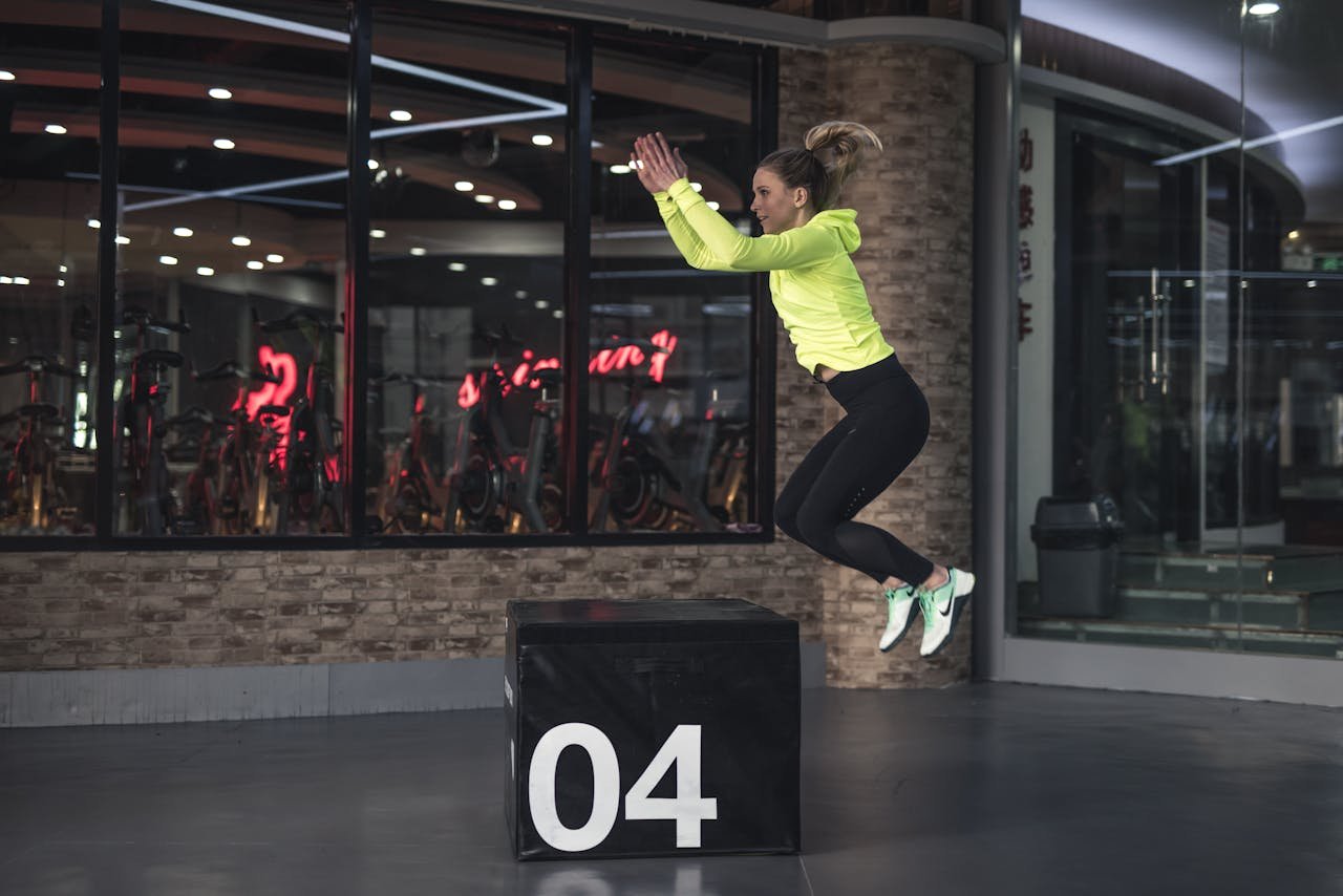 services-02 Fit young woman in sports wear executing a box jump indoors, promoting fitness and health in a modern urban gym.